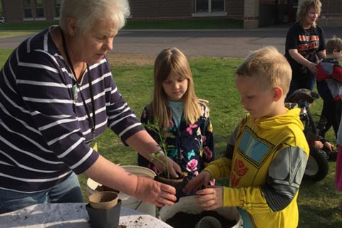 Lynn Adams helping children with a potted plant as they all stand outside with a bucket of dirt